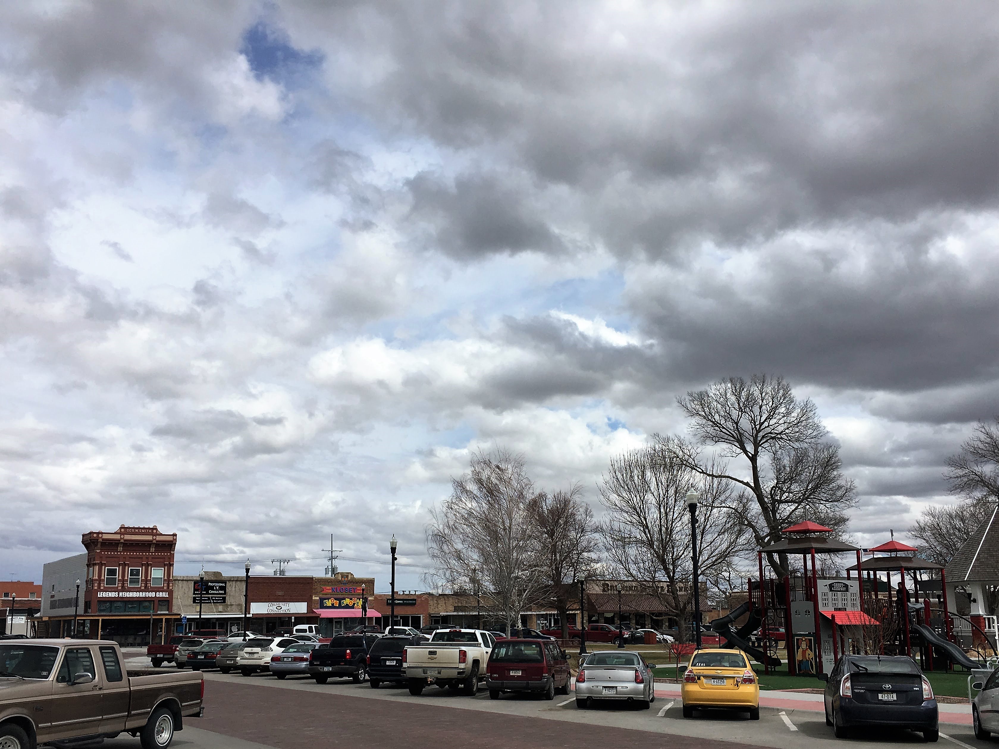 A sky full of clouds over top of a small town Main Street with cars and quaint buildings.