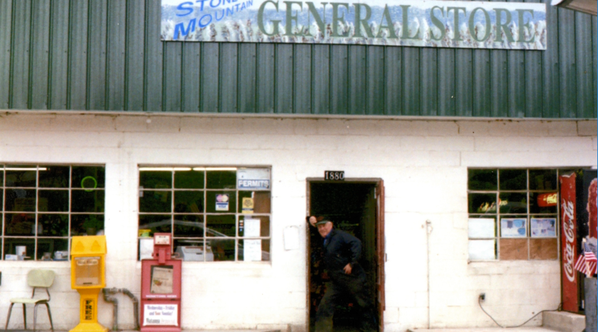 A man stands in the doorway of a small white building with a sign over the door that reads, Stone Mountain General Store.