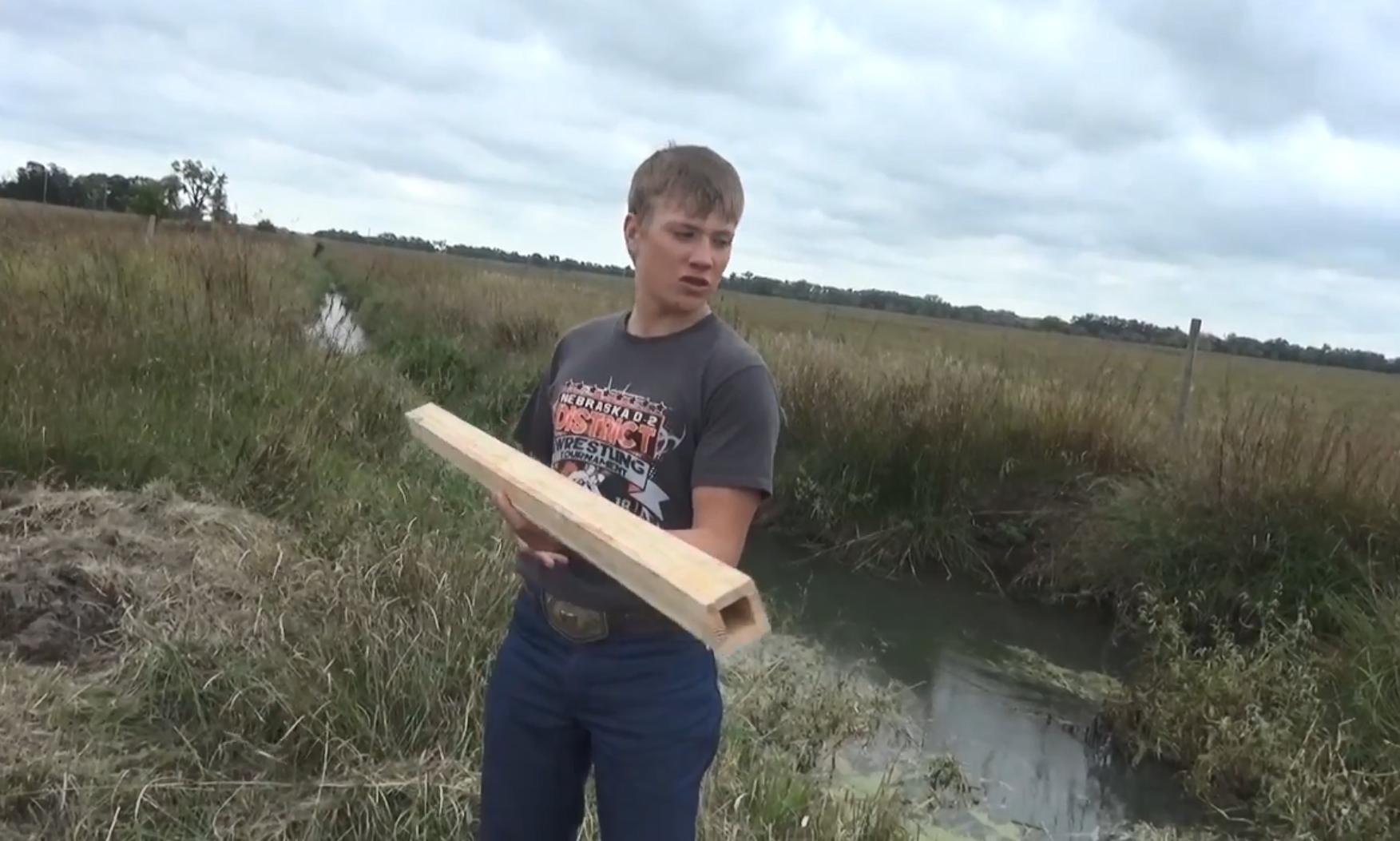 A young boy holds a wooden pipe near a wetlands area in Nebraska.