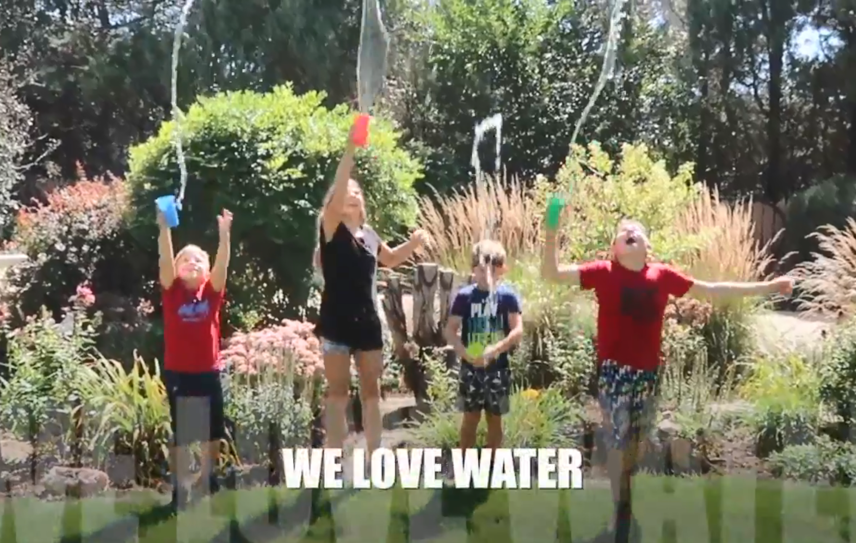 Four children jump in the air as they throw cups of water on each other.