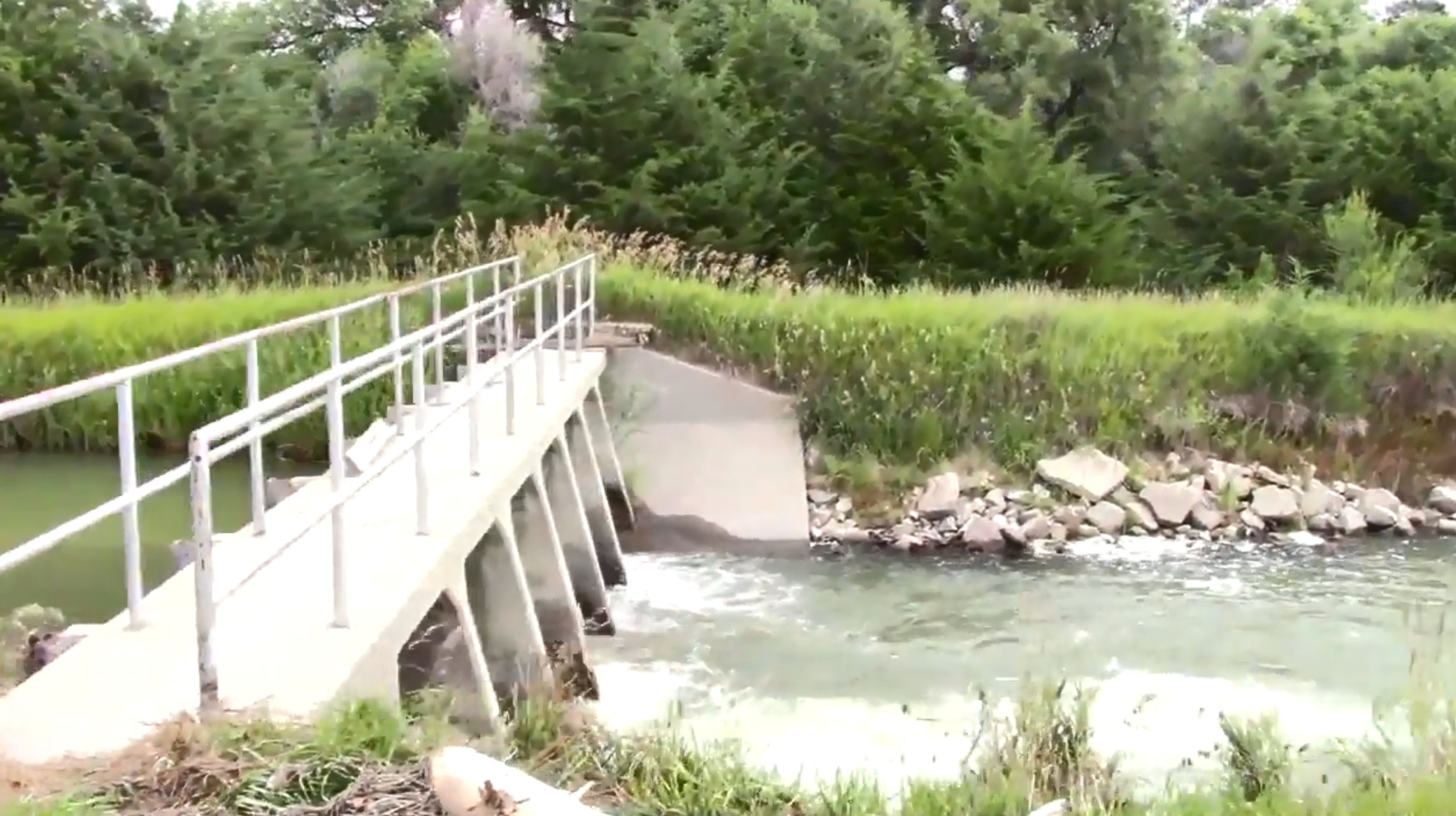 A narrow concrete walkway spans a small river.