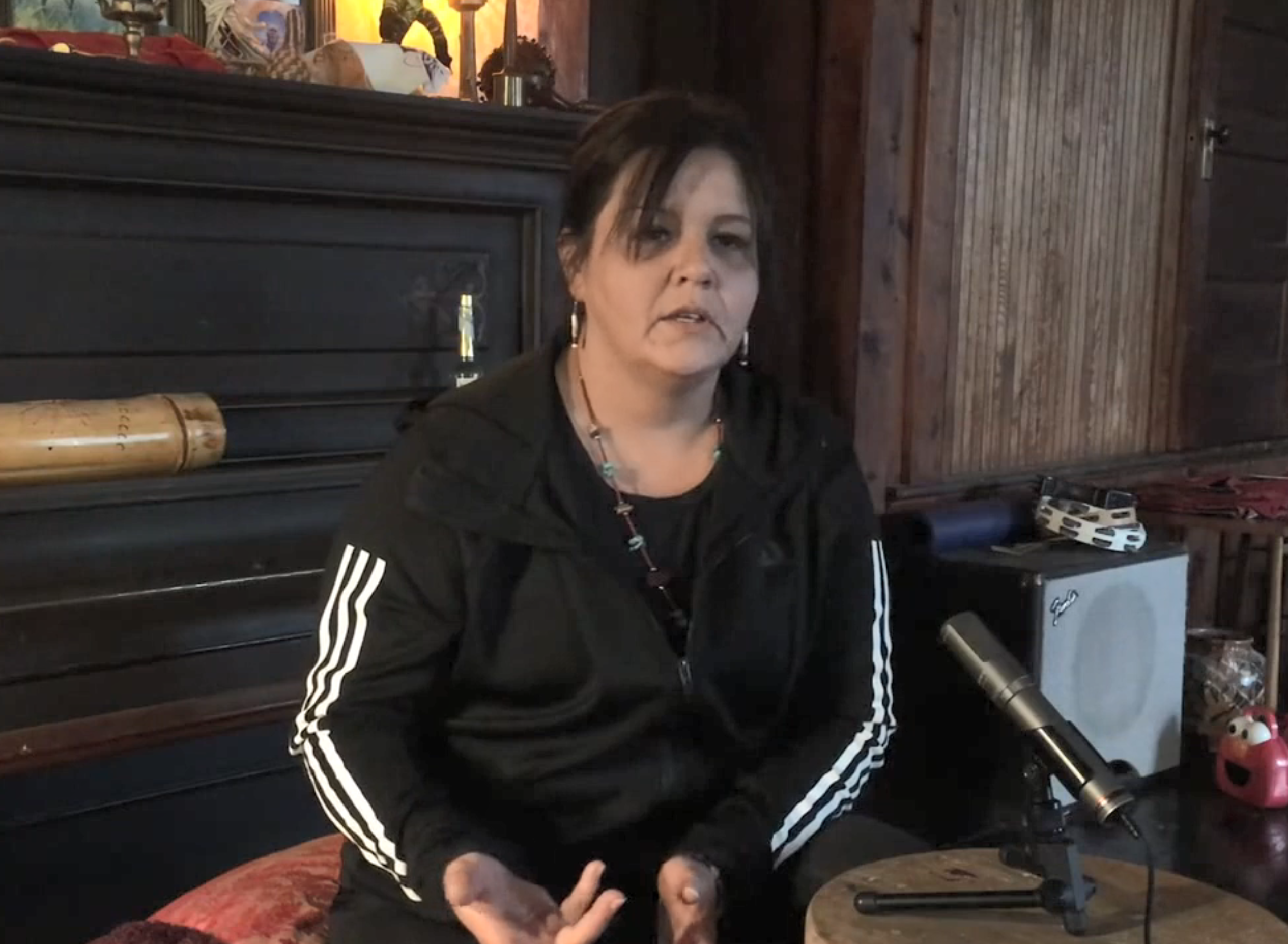 A woman with brown hair and a black running jacket sits in front of a microphone in her home. 