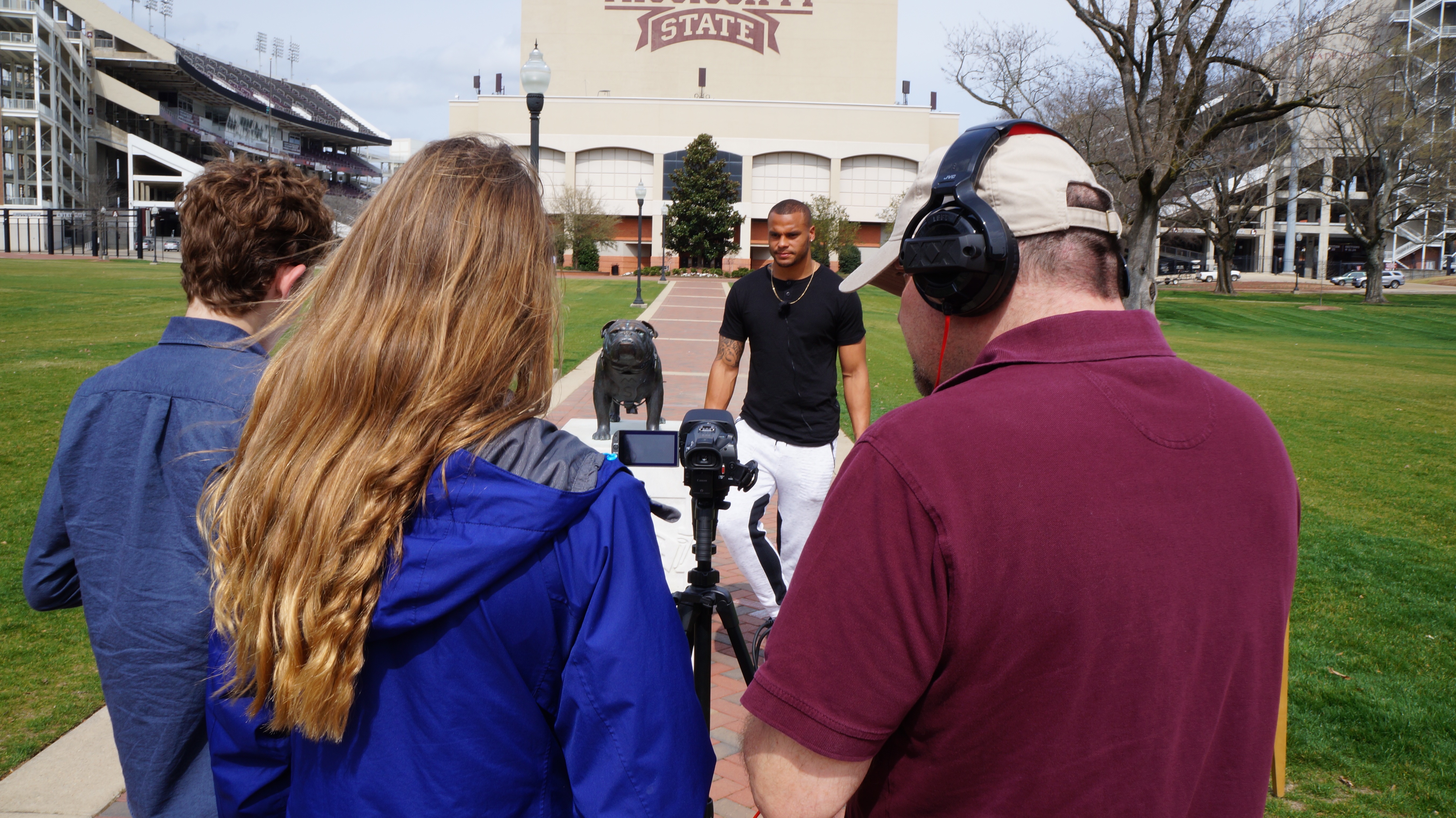 Three students, carrying video recording equipment, interview a young athlete on the campus of a college.