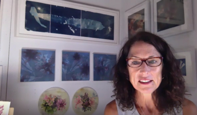 With brown hair and glasses, Mary sits in her studio with the walls covered with blue artwork.