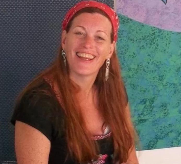 A woman with long brown hair and a red bandana smiles at the camera.