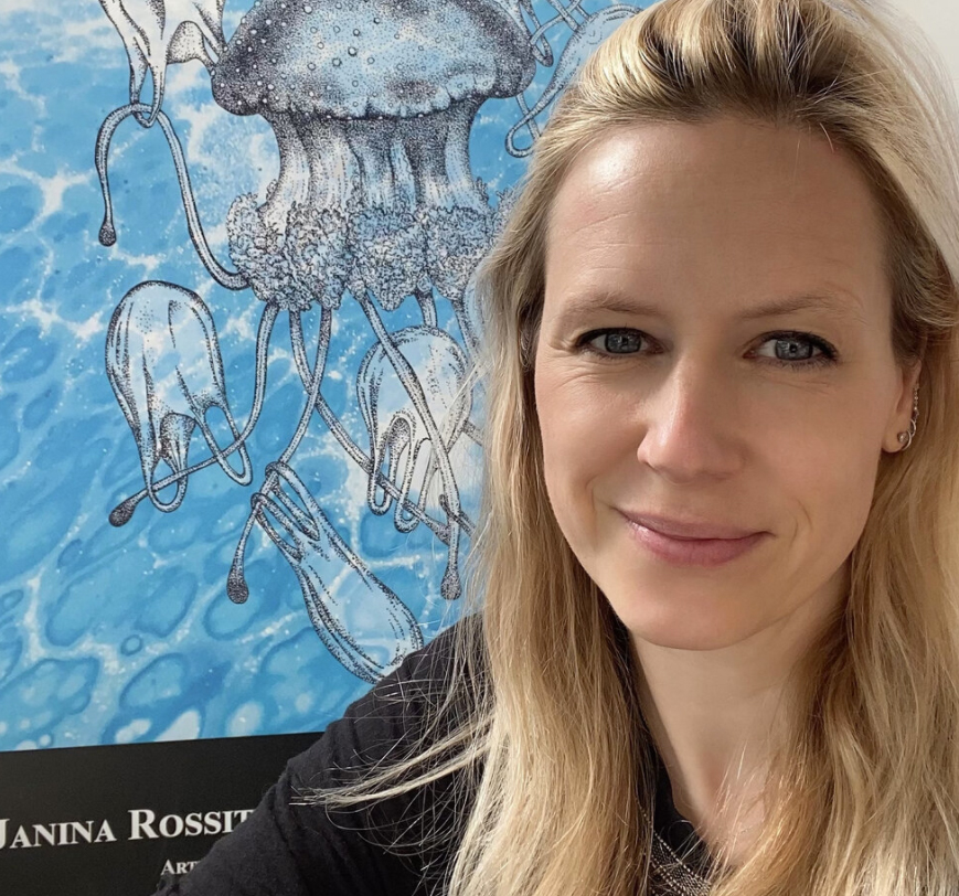 Nina has long, blonde hair and black shirt. She sits in front of artwork with black and white jellyfish.