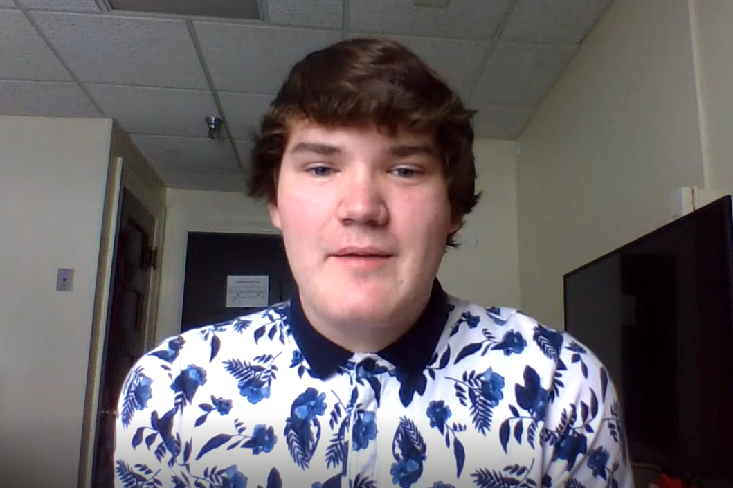 Reeve has short brown hair and a collared shirt, with blue flowers and patterns on it.