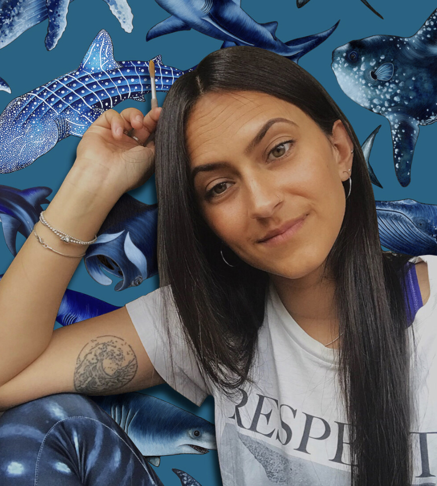 Janavi has long, straight black hair and a white t-shirt on. She sits in front of a painting of sharks.