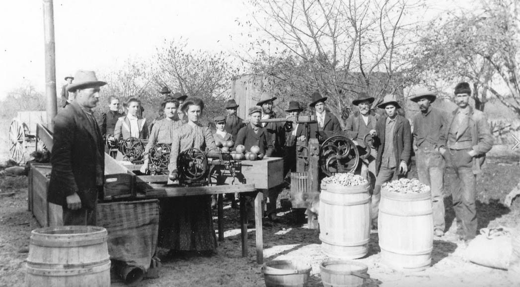 Vintage image of people in farm clothing standing around a market where foods and other goods are on display or for sale..