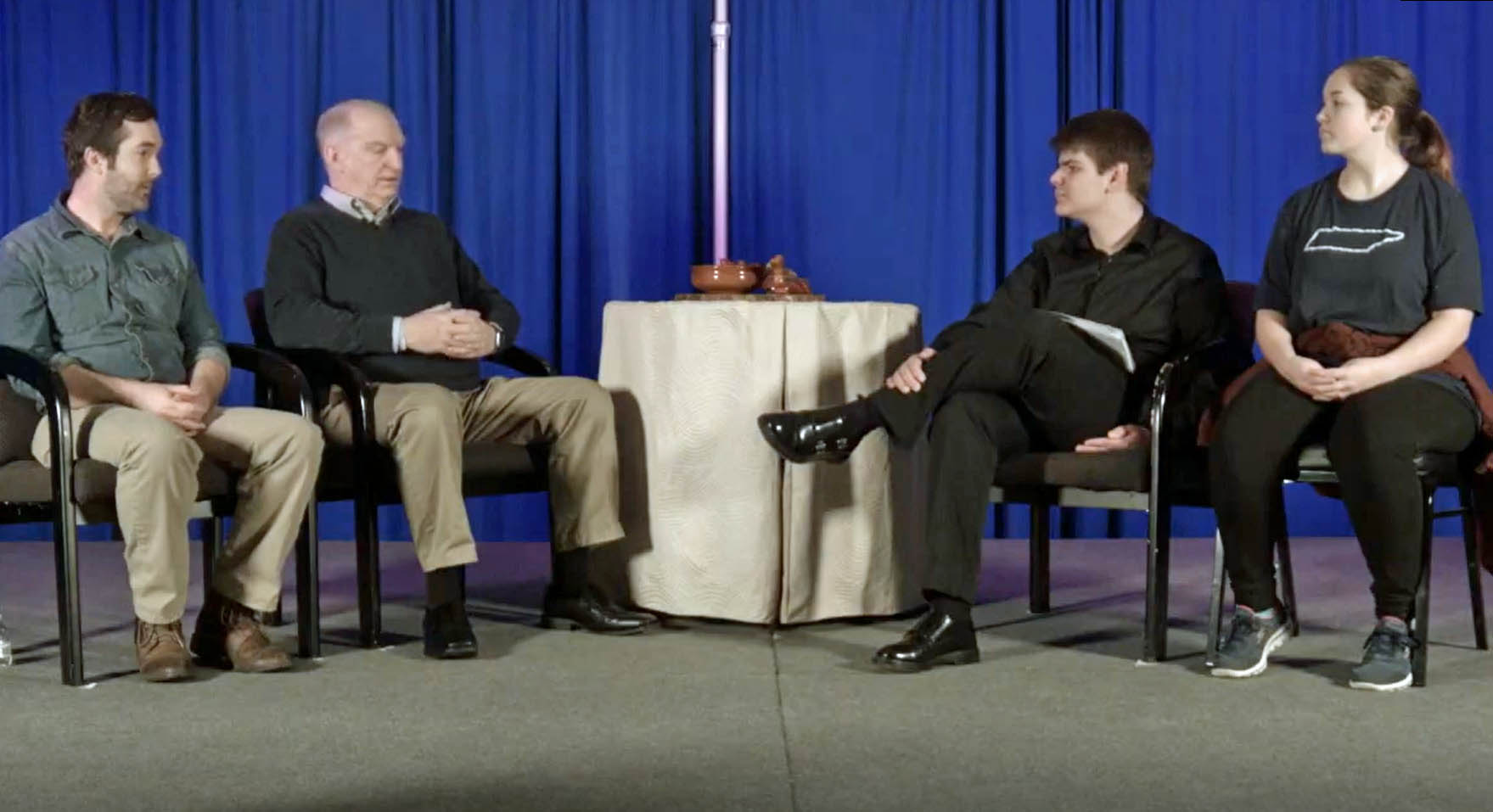 Four people sit on a stage--two students and two adults--in an interview setting.