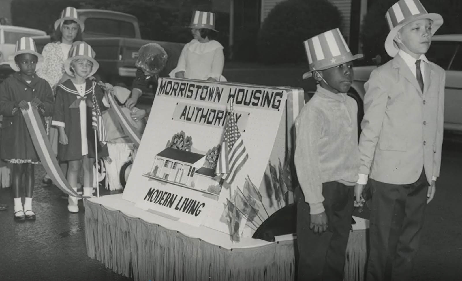 Small children wear Americana top hats and participate in a 1960s parade. 