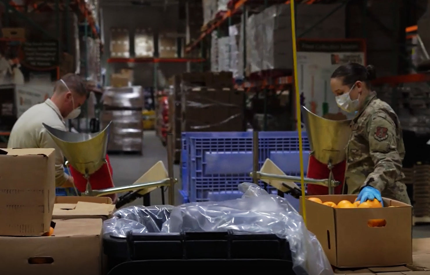 Two people wearing army fatigues load supplies in boxes in a warehouse.