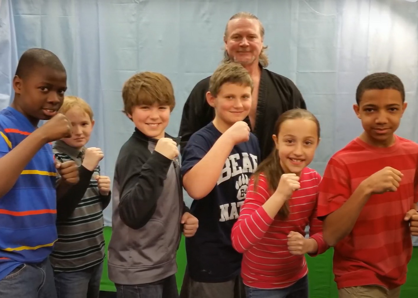 Children stand around a karate instructor and make a fist in support. 