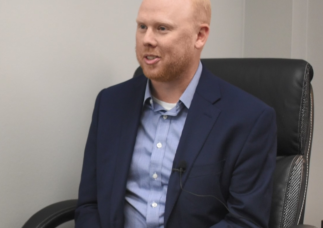 A man with red hair and blue blazer sits in a black leather chair.