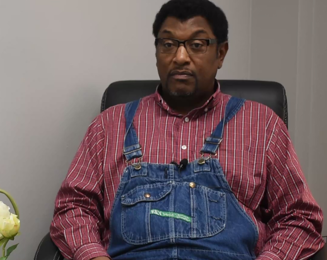 Jimmy wears a red, plaid shirt and blue jean overalls. 