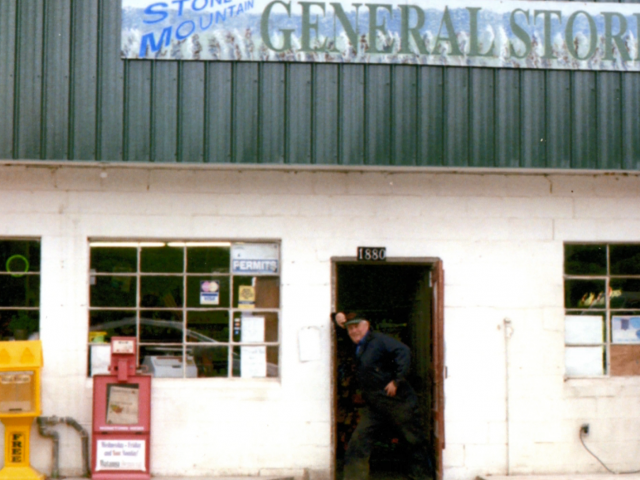 A man stands in the doorway of a small white building with a sign over the door that reads, Stone Mountain General Store.