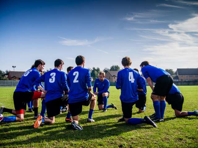 A group of teens in blue soccer uniforms huddle in a circle. Pexels stock photo.