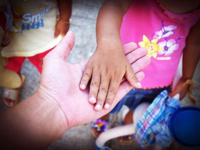 A person holds out their hands to a small child who places her hand in theirs. 