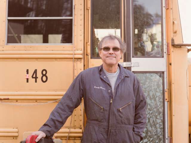 Randy Henson stands in front of a school bus. 