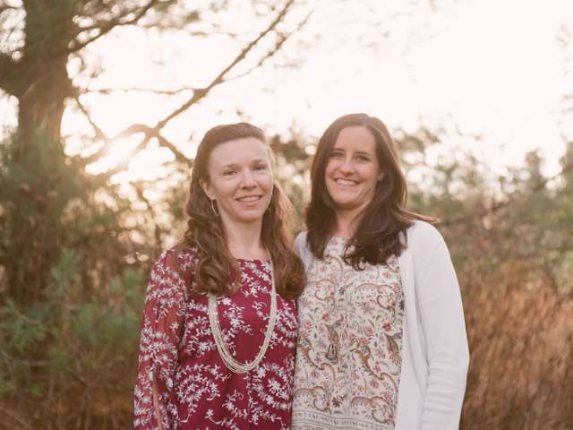 Allison and Samantha stand outside in a wooded area.