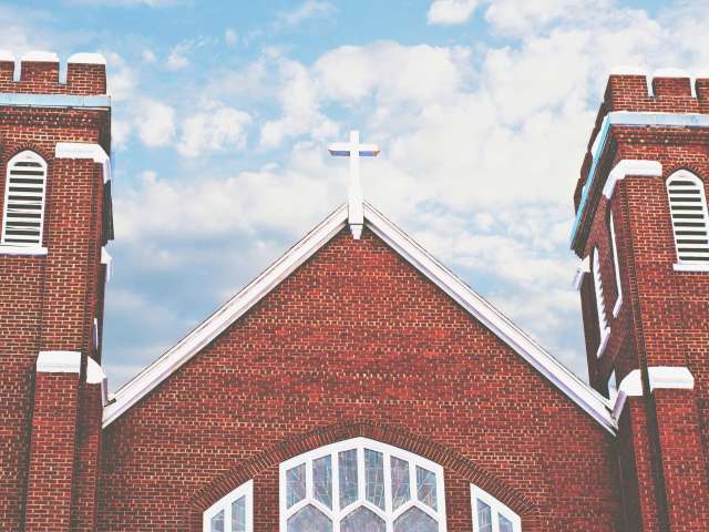 A view of two towers and the central window of a red brick church. Pexels stock photo