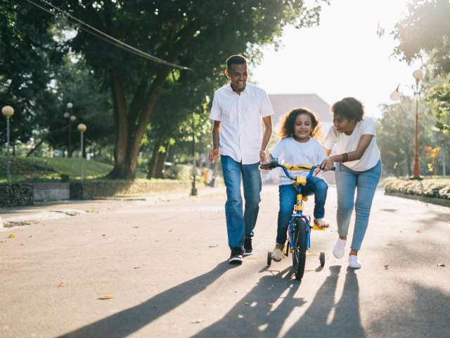 A girl rides a bike as her parents help her learn to ride. Pexels