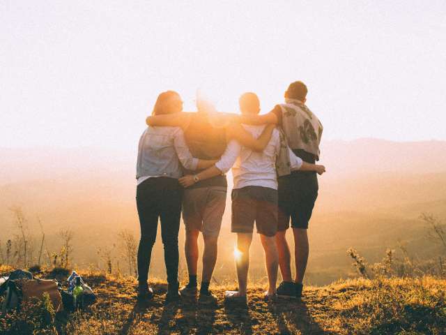 A group of four friends stand on a horizon lit by the sun. Pexels stock photo.
