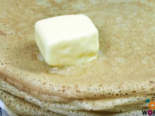 A stack of pancakes on a plate with a square patty of butter melting on top of them. 