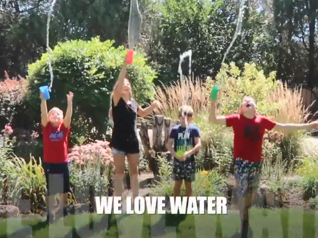 Four children jump in the air as they throw cups full of water on each other.