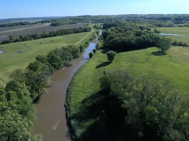 Little Blue River aerial shot, showing a winding brown river with trees and green fields on either side.