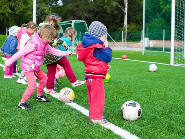 A group of toddlers run with soccer balls on a green field. Pexels photo.