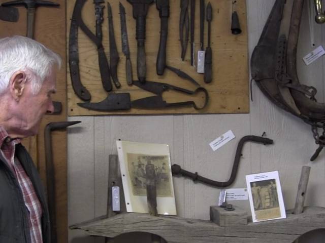 A man looks on to a table and wall filled with old tools in a museum exhibition space.