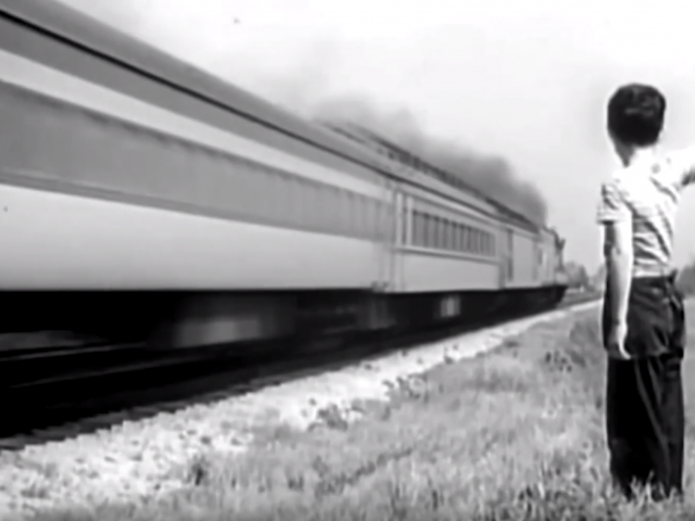 In a vintage photo, a boy stands beside a speeding train and waves.