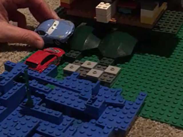 A woman moves a toy car around on a Lego board. Screenshot from video.