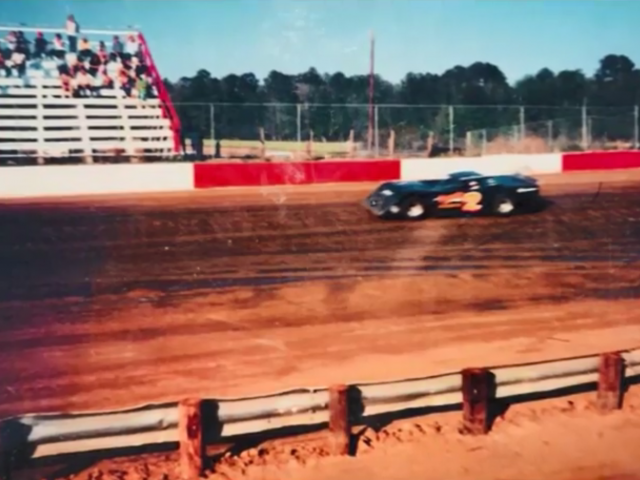 A vintage photo of a dirt motor speedway with a car and people in the stands watching. 