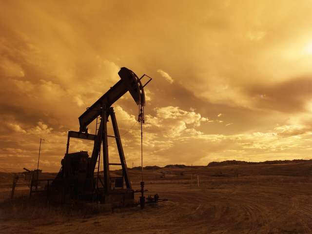 An old-fashioned oil rig bobs up and down on a dusty, flat ranch.