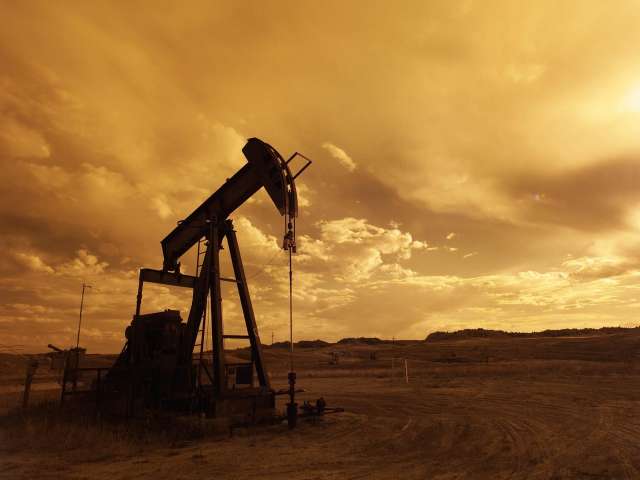 An old-fashioned oil rig bobs up and down on a dusty, flat ranch. 