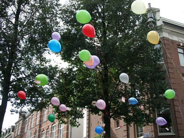 Colorful ballons fly off into the sky beside a small-town brick building. 