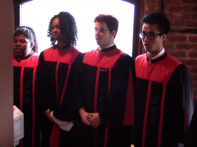 A group of high school choir students wear black and red robes.