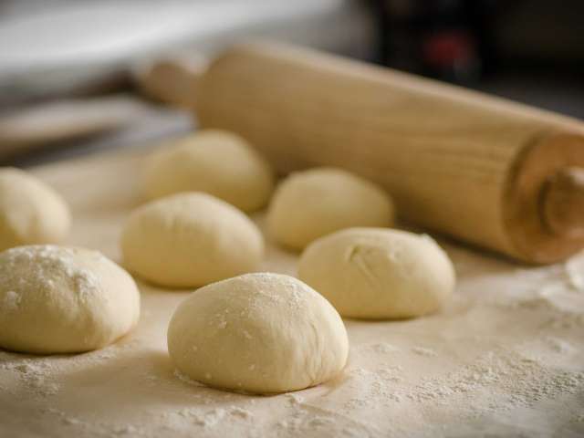 Balls of dough rest on a counter top with a rolling pin. 