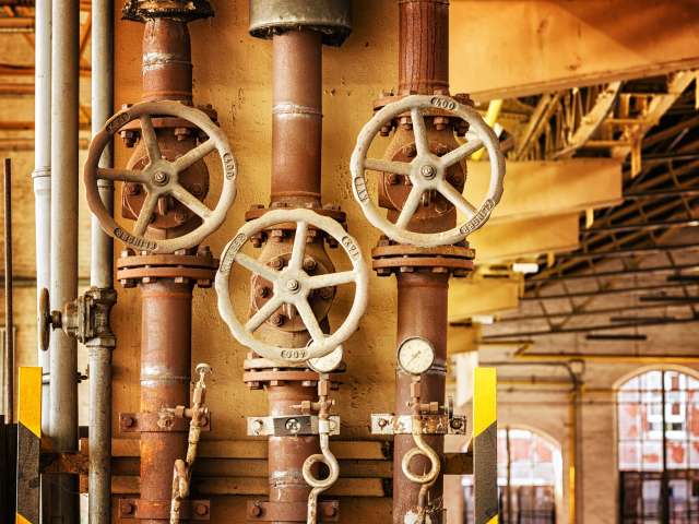 Three rusty wheel valves inside a large industrial plant. 