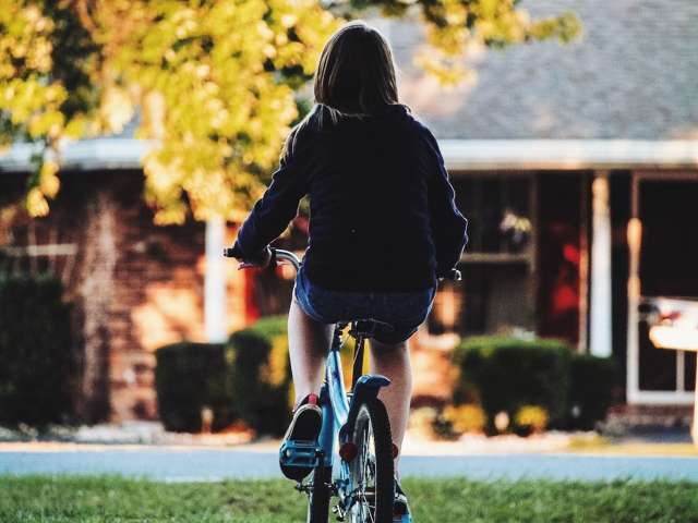 A girl rides away on a bicycle on a fall day.