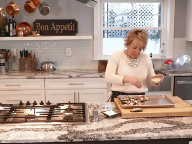 A woman stands in a gourmet kitchen and makes crab cakes. 