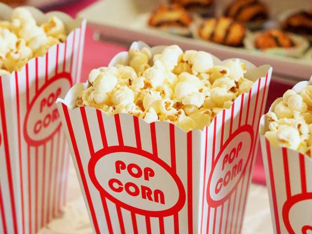 Three containers of movie popcorn in a class red and white, striped popcorn cup. 