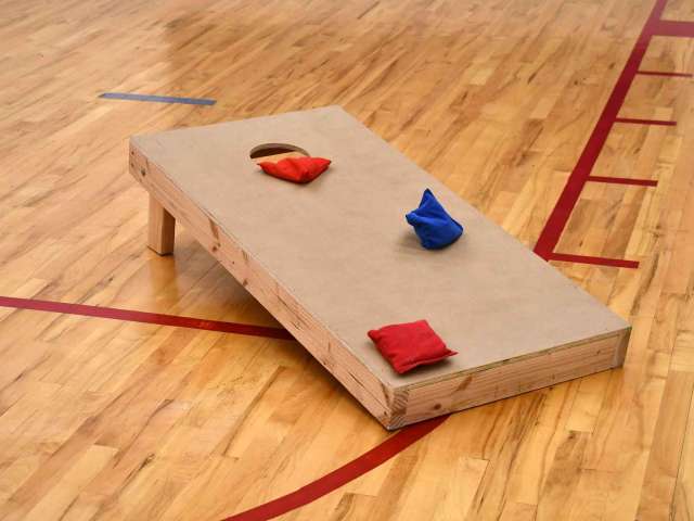 A wooden corn hole board with three bean bags on it in a school gymnasium. 