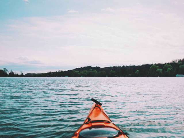 The tip of an orange kayak gliding through the water. 