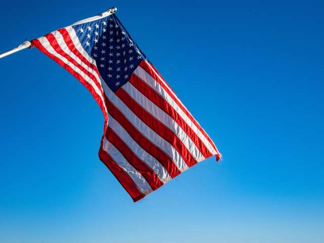 An American flag waves in the sky on a clear day. 