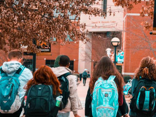 A group of teens walks toward a brick school building. 