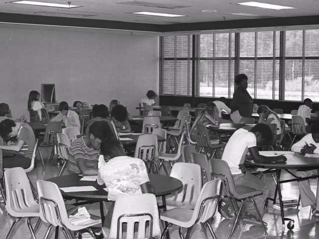 A vintage photo of African American children in a classroom space with small chairs and tables.