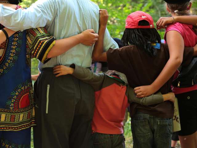 A group of adults and young peope put their arms around each other in a circle. 